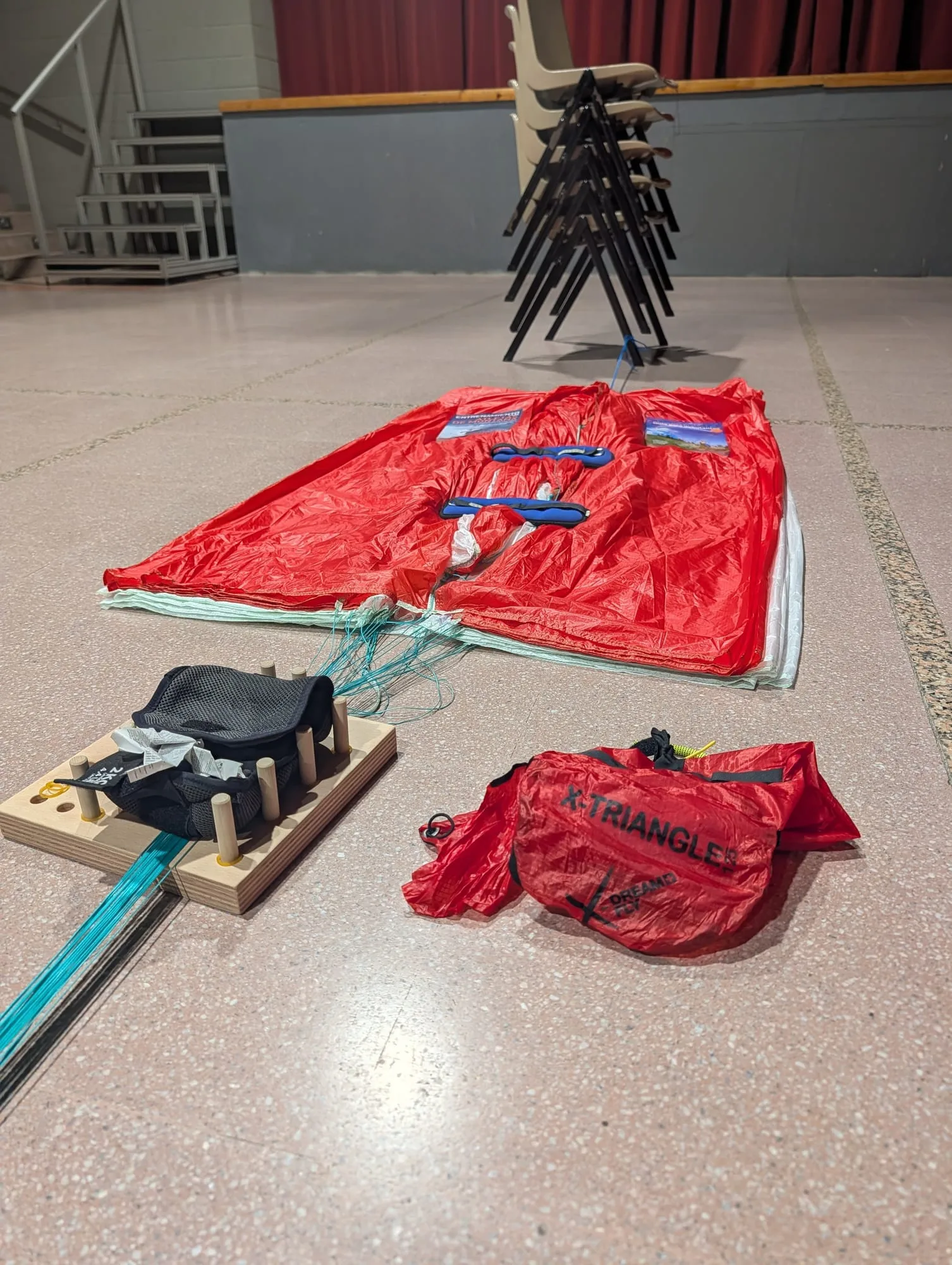 Vista general del plegado: el paracaídas extendido al fondo, el tablero de plegado con las líneas en primer plano y una bolsa roja al lado
