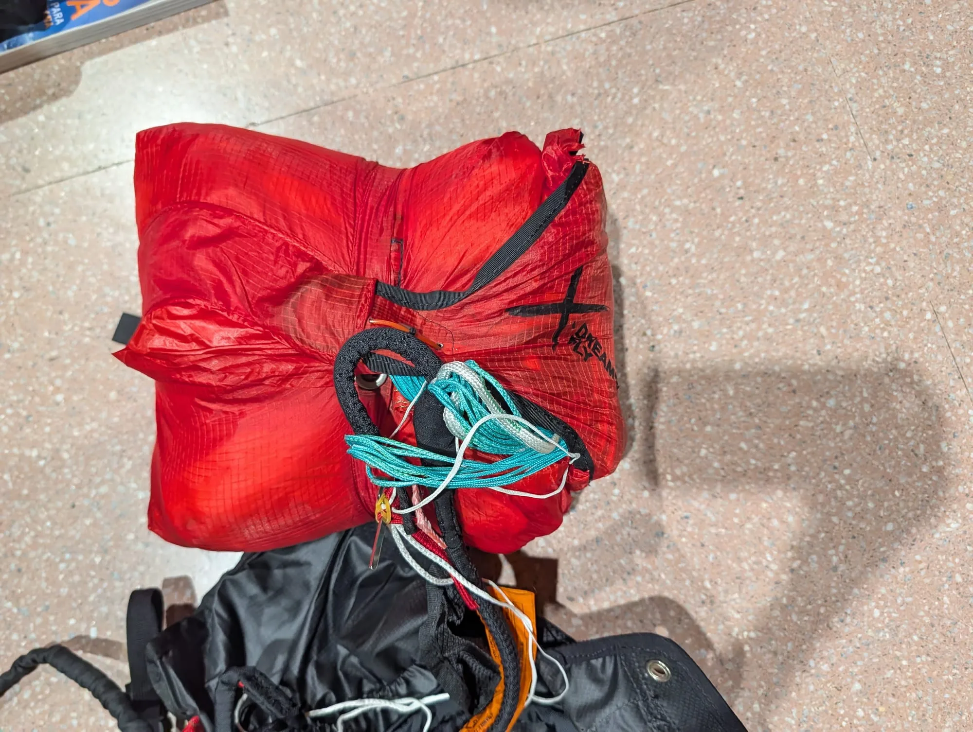 Primer plano del paracaídas de emergencia rojo plegado, con la brida y los cordones recogidos encima, junto a la silla
